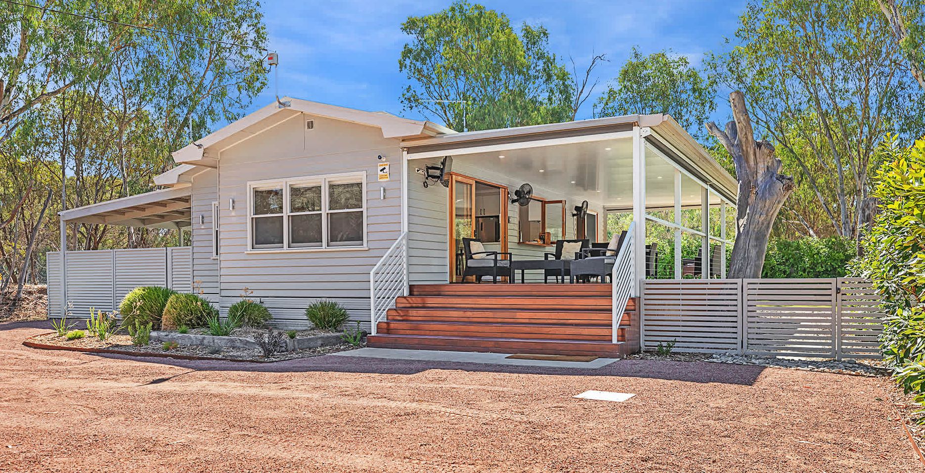 Ein modernes Einfamilienhaus mit verdeckter Veranda, einer Treppe zum Eingang und einem angelegten Garten mit Kakteen und Sträuchern.