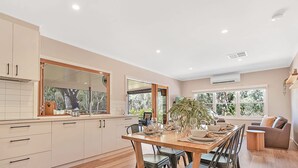 Een moderne keuken met witte kasten, een groot raam en een eethoek met een tafel voor vier personen.