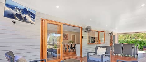 A modern outdoor living area with a dining table, chairs, and a large TV screen displaying a mountain view.
