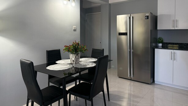 A modern kitchen with a stainless steel refrigerator, white cabinets, and a dining area with a table set for four. - Hilltop Condos Unit 3 - 1-bedroom with AC, WiFi centrally located in Gros Islet (Gros Islet)