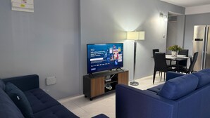 A modern living room with a flat-screen TV, a dining area with a table and chairs, and a blue sofa. - Hilltop Condos Unit 3 - 1-bedroom with AC, WiFi centrally located in Gros Islet (Gros Islet)