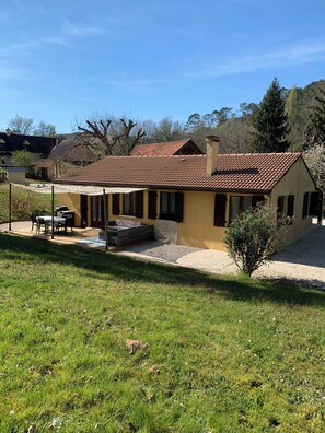 Uma casa térrea com telhado de cerâmica, um pátio com móveis de exterior e uma pequena área de jardim.