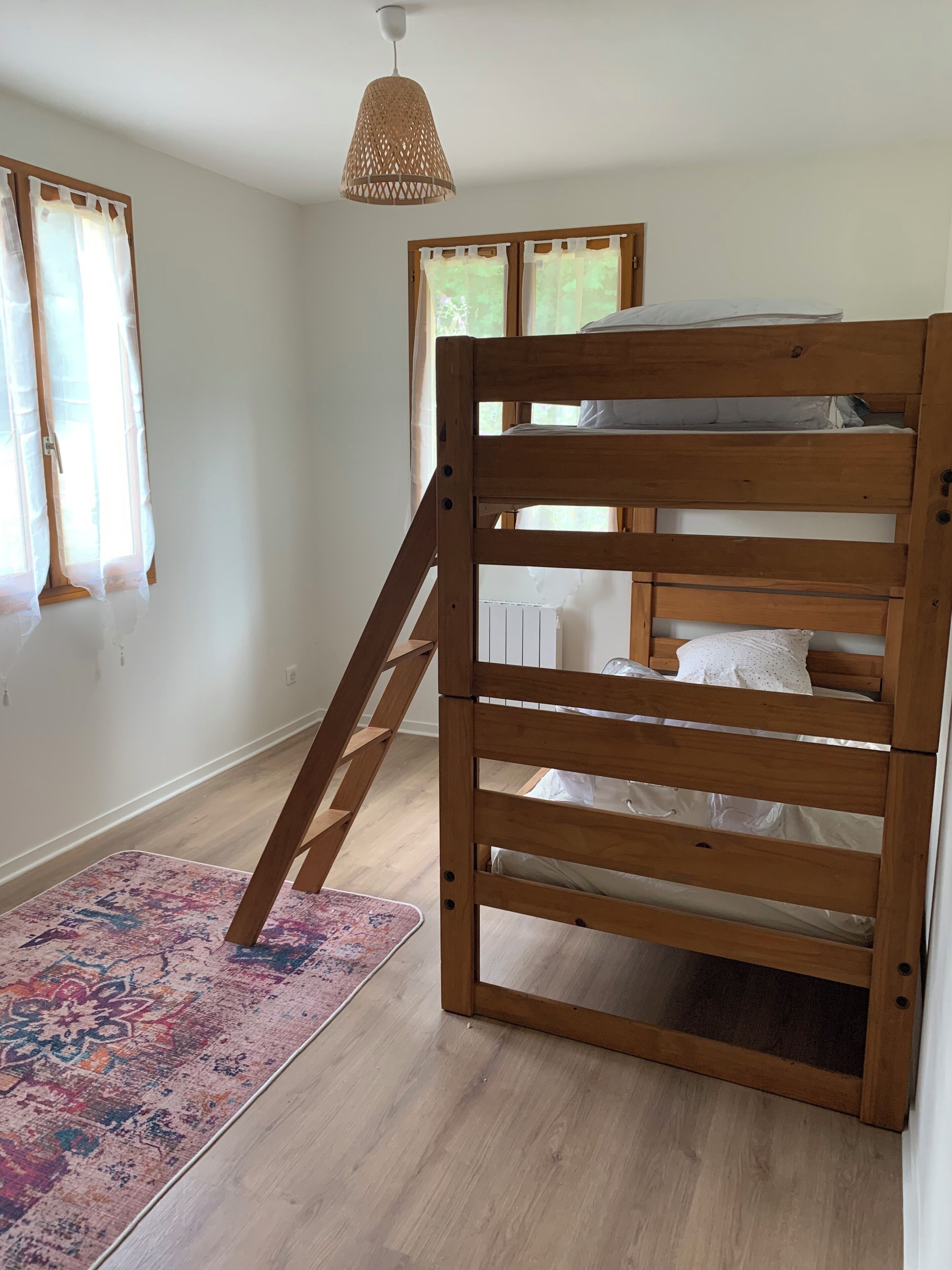A bunk bed with a wooden ladder, a woven pendant light, and a patterned rug.