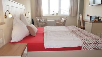 A bedroom with a bed, bedside tables, a chair, a desk, a television, and a window with curtains.