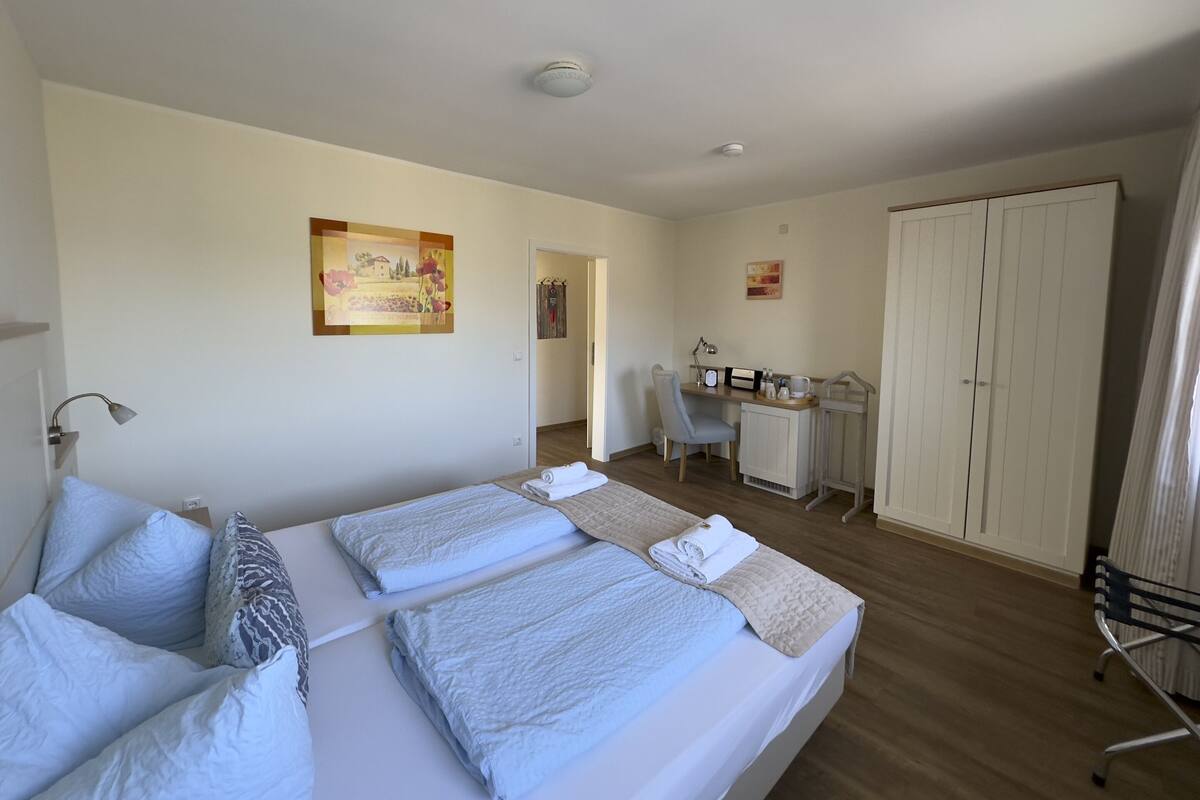 Ein Hotelzimmer mit zwei Betten, einem Schreibtisch, einem Stuhl, einem Kleiderschrank und einem Bild an der Wand.