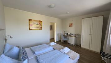 A hotel room with two beds, a desk, a chair, a wardrobe, and a painting on the wall.