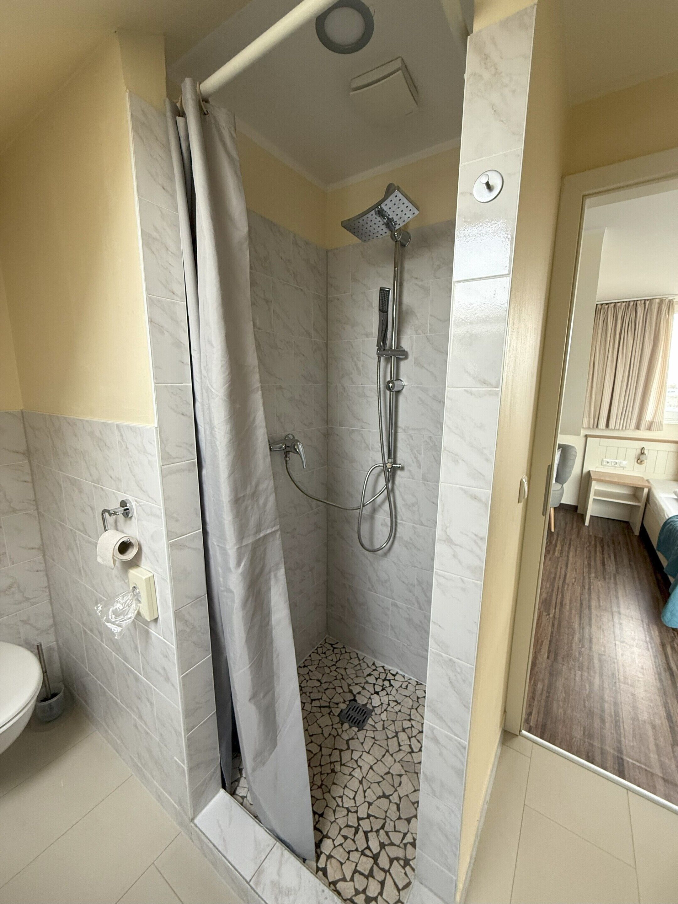 A shower area with a marble floor, a showerhead, and a curtain.