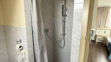 A shower area with a marble floor, a showerhead, and a curtain.