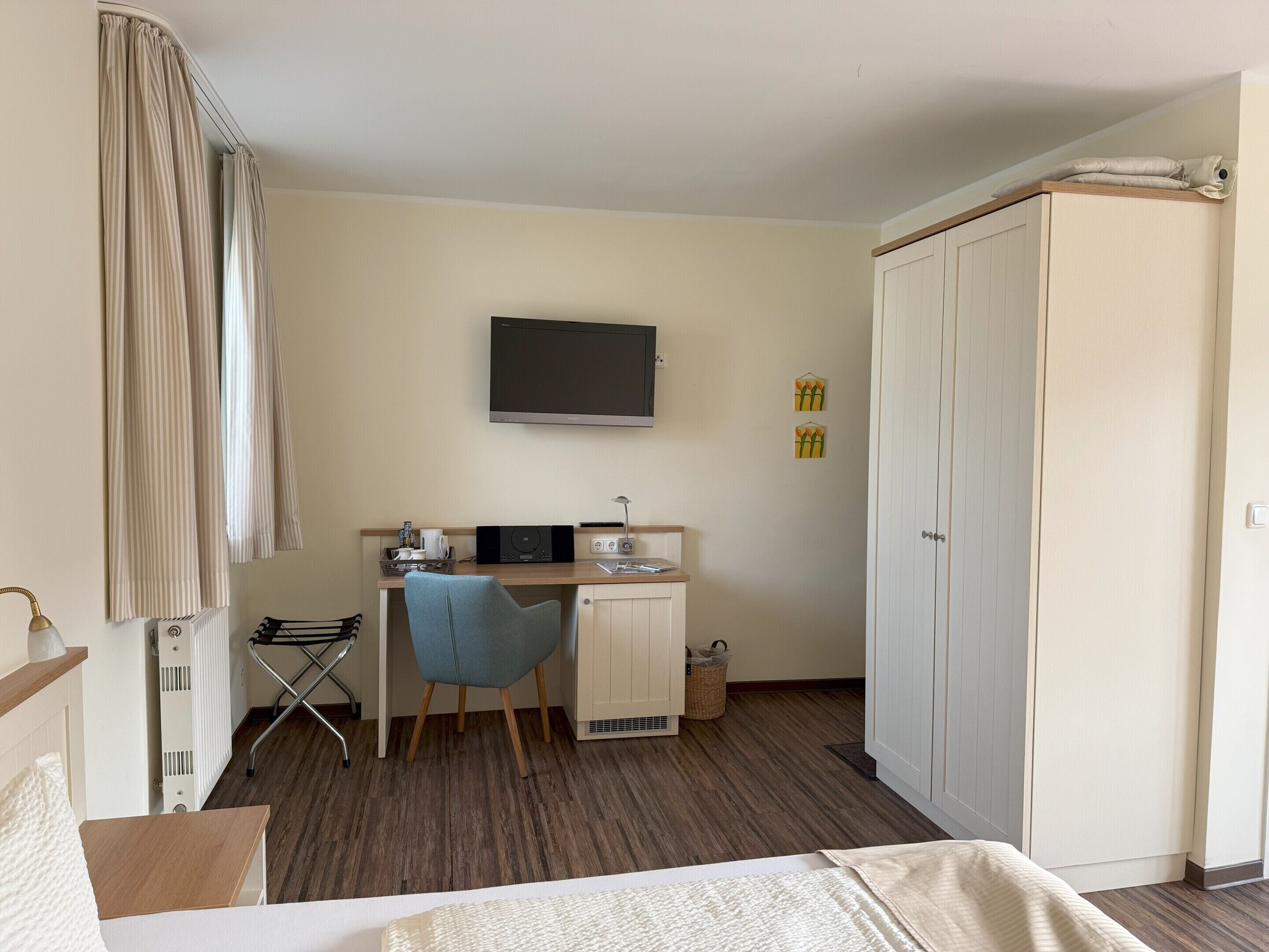 Habitación de hotel con cama, escritorio con silla, televisor, armario y radiador.