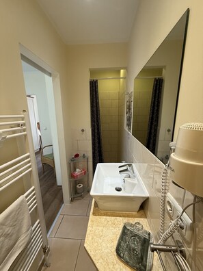 A bathroom with a white sink, a mirror, a towel rack, a shower curtain, and a toilet. - Pension Walmeer (Kellenhusen)