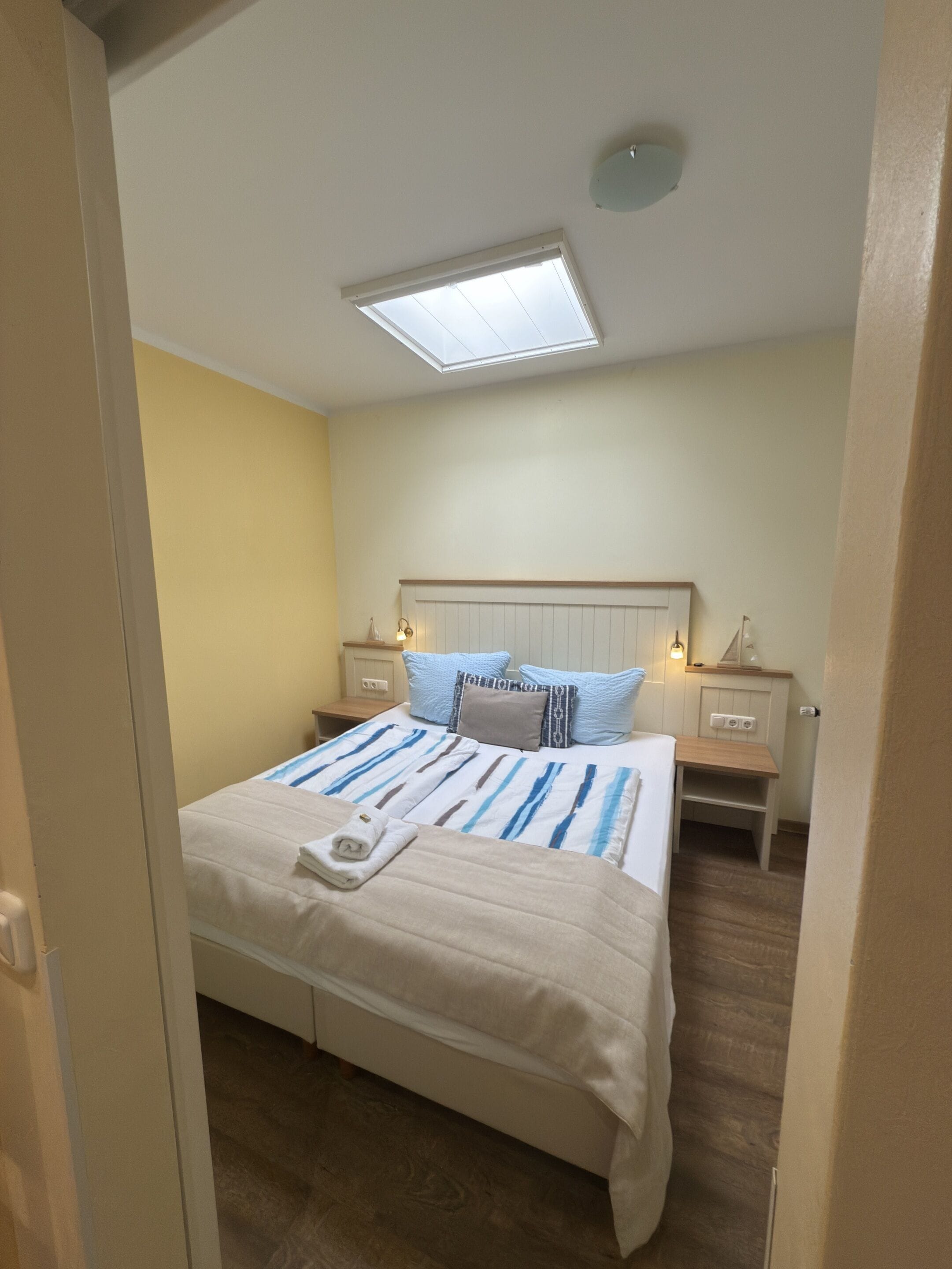 Une chambre à coucher comprenant un lit, des tables de chevet, une commode, un luminaire au plafond et un puits de lumière.