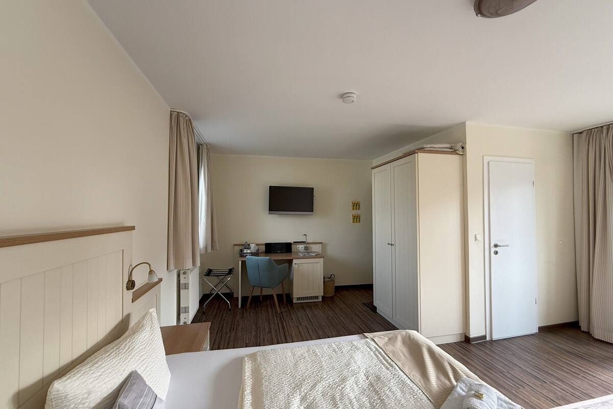 Ein Hotelzimmer mit Bett, Schreibtisch, Stuhl, Fernseher und Kleiderschrank.