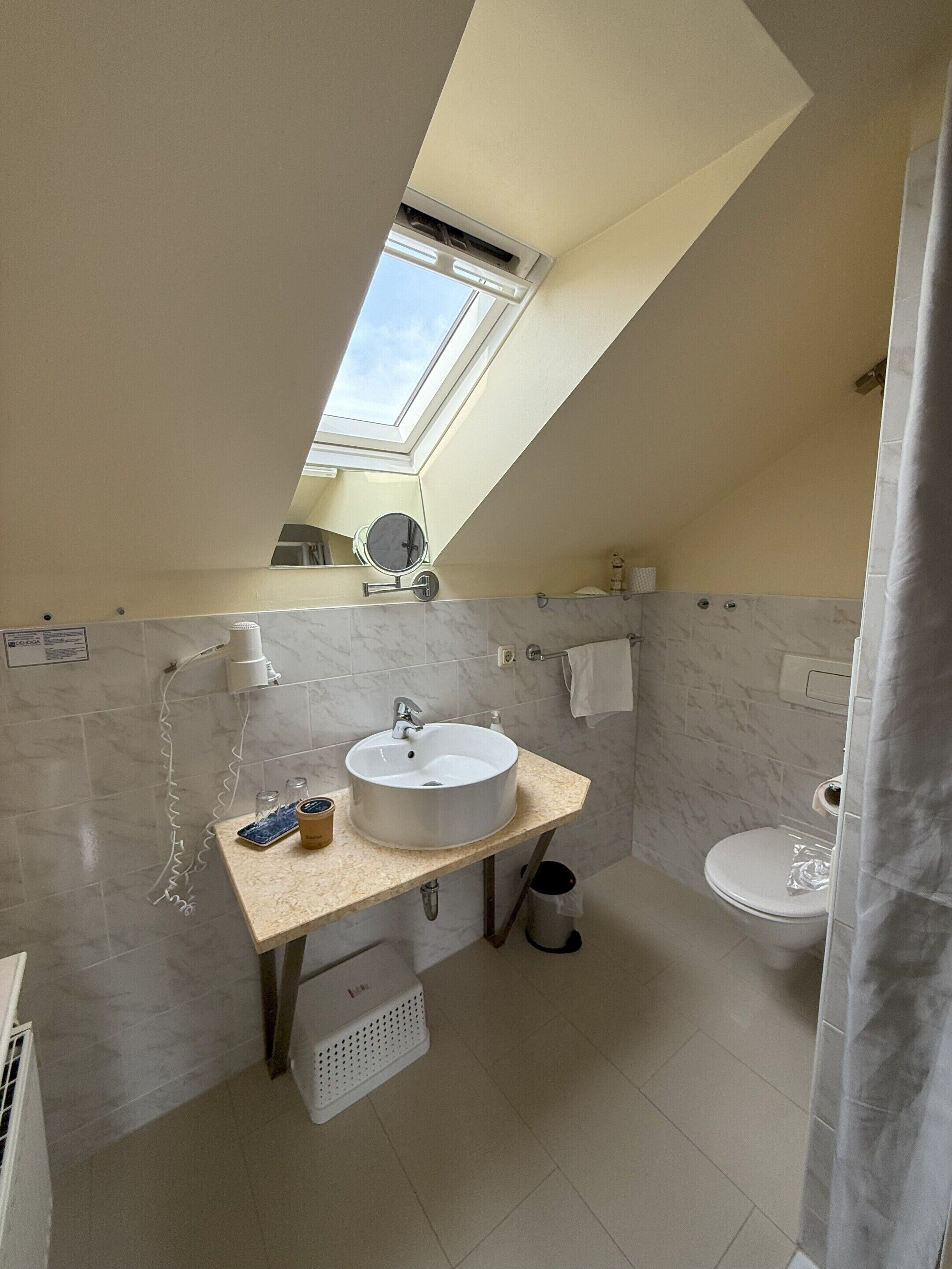 Et moderne badeværelse med ovenlys, håndvask, toilet og bruseforhæng.