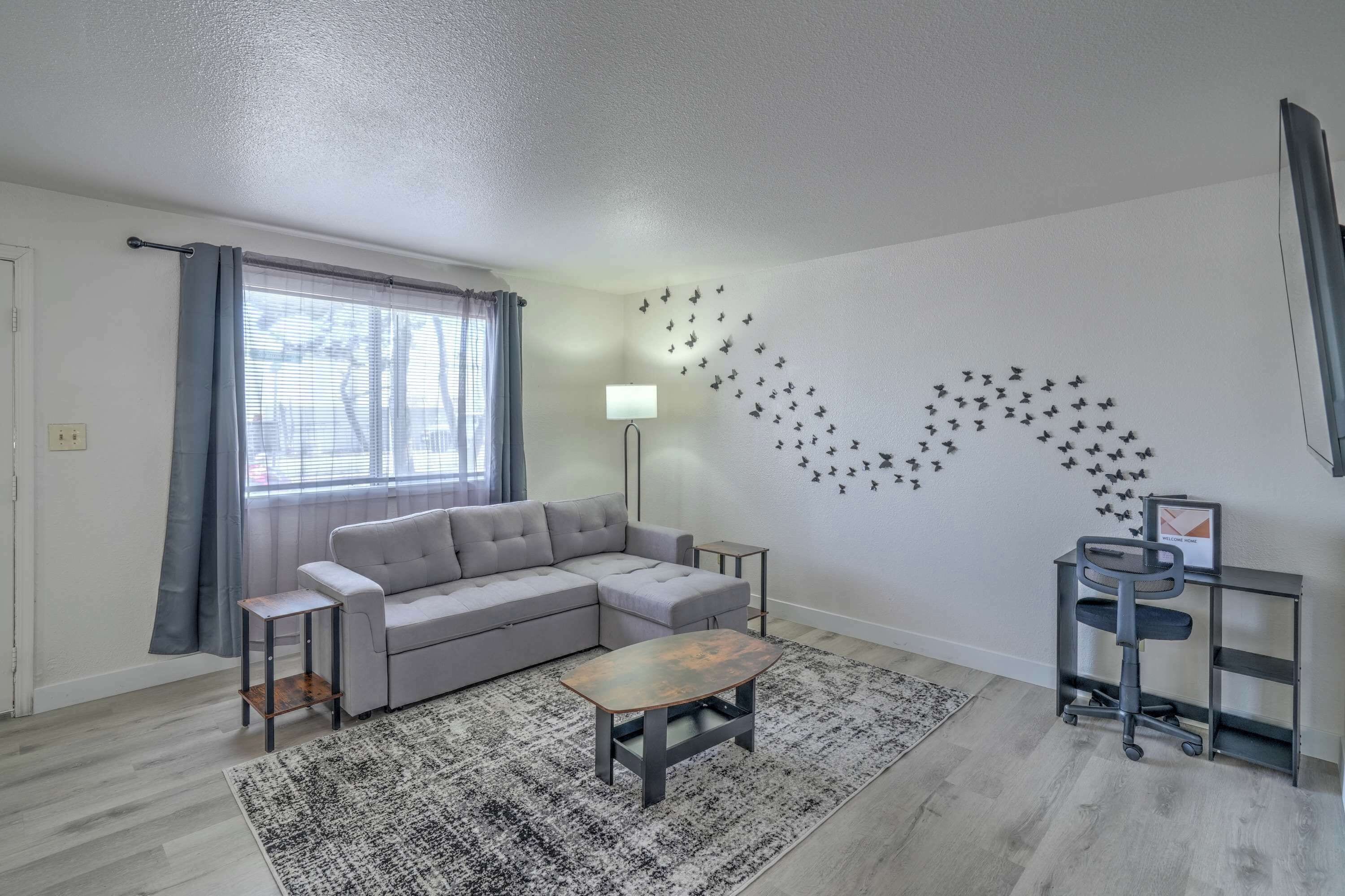 A modern living room with a grey sectional sofa, a small wooden coffee table, a standing lamp, and a wall-mounted shelf with a chair.