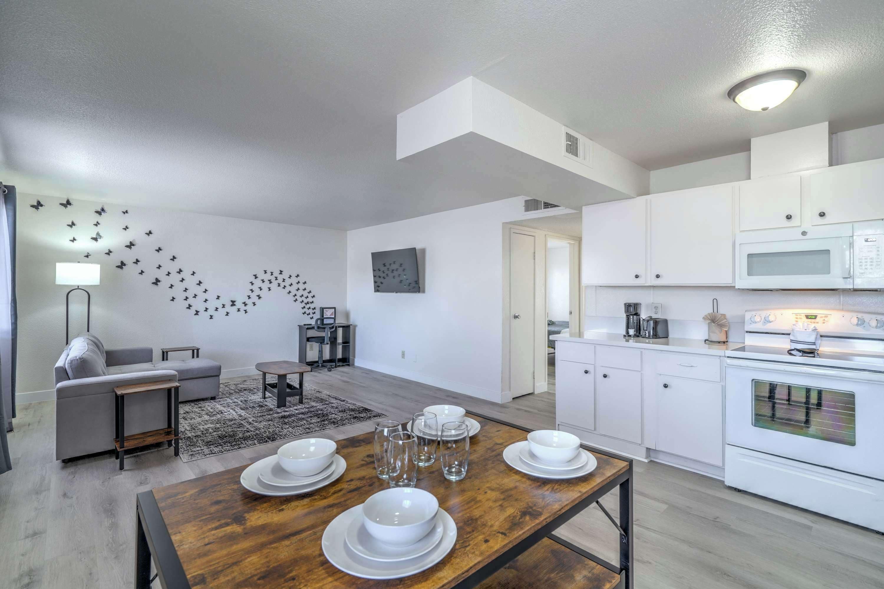 A modern kitchen with white cabinets, a microwave, and an oven. There is a dining table set with plates and glasses.