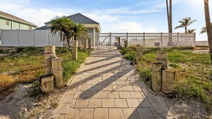 Ein gepflasterter Weg führt zu einem befestigten Bereich mit einem Haus und Palmen.