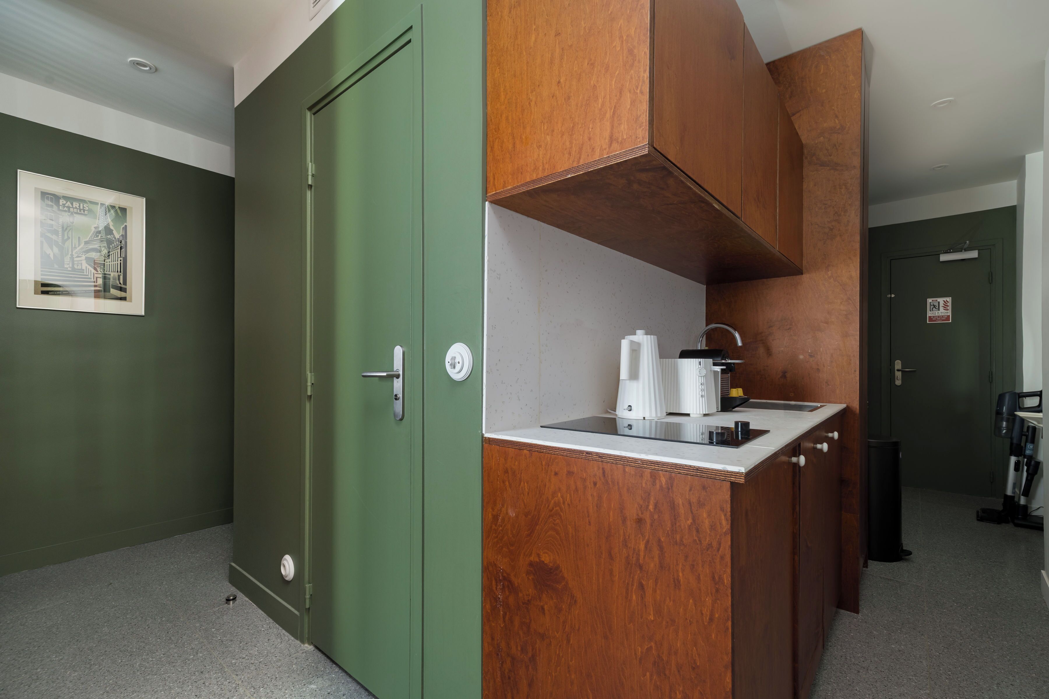 Een kleine keuken met een groene deur, een houten aanrecht en een koffieapparaat.