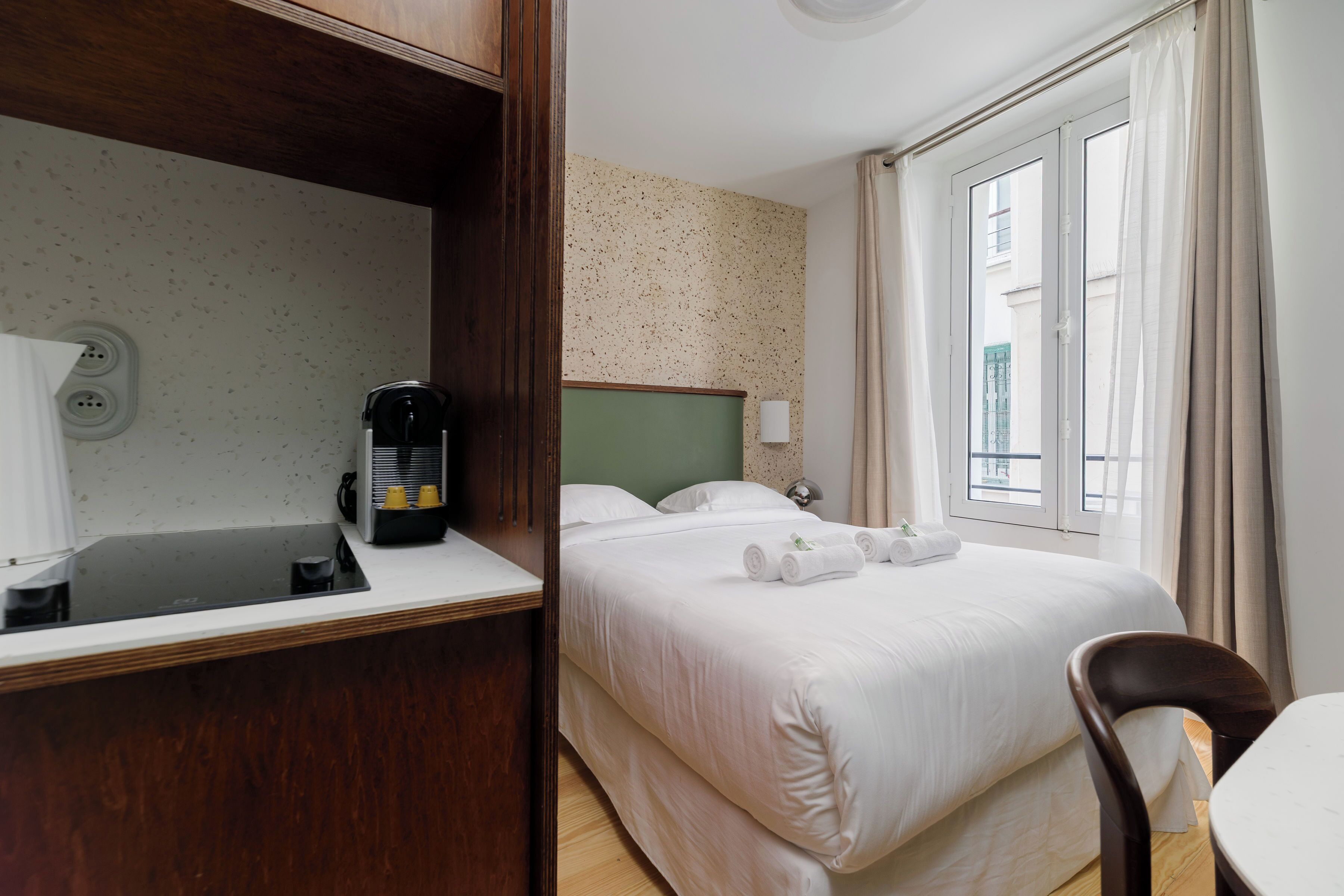 Una habitación de hotel con cama, escritorio, cafetera y ventana con cortinas.