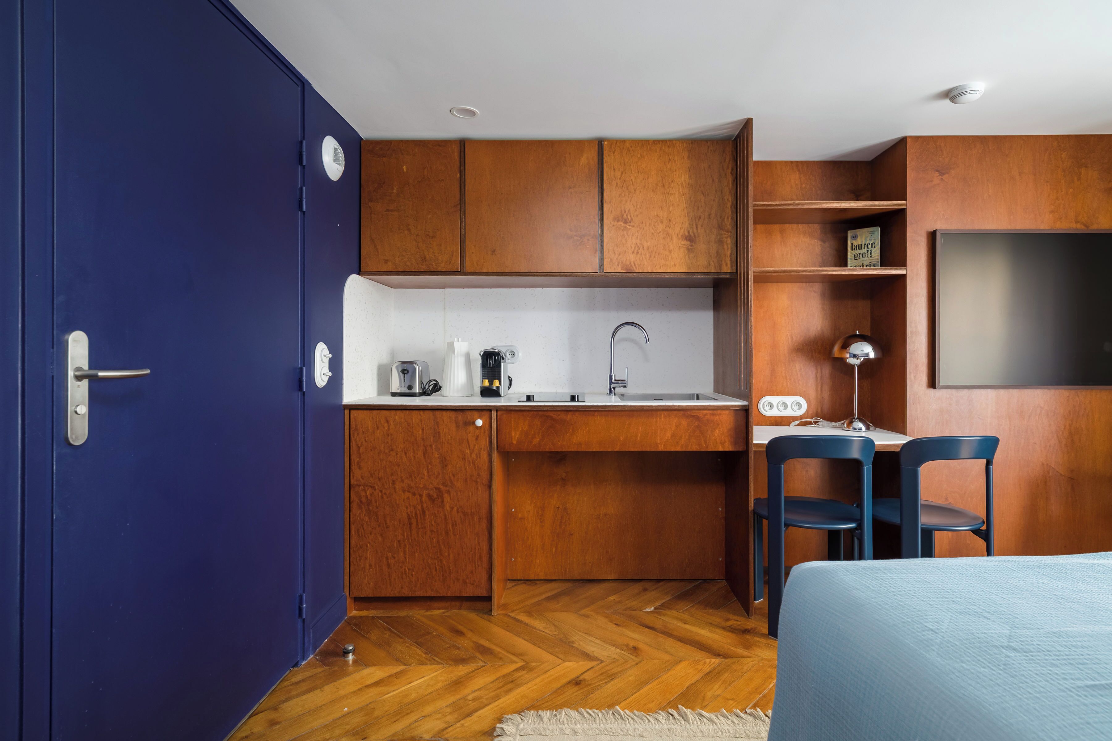 A compact room with a kitchenette, a bed, and a desk with chairs.