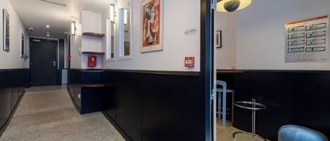 Ein Flur mit Wand in Schwarzweiß, einer blauen Bank, einem kleinen Tisch und einem roten Rauchmelder.