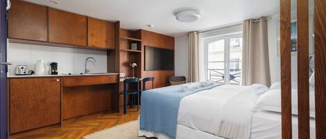 Een kleine hotelkamer met een kitchenette, een bed, een bureau en een stoel.
