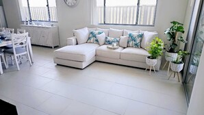 Un salon moderne avec un canapé d’angle blanc, une table à manger avec des chaises et des plantes en pot.