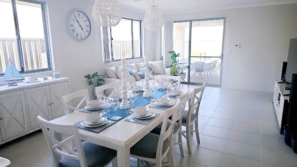 Un coin repas avec une table blanche dressée pour six personnes, entourée de chaises blanches.