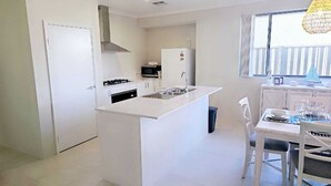 Une cuisine moderne avec des meubles blancs, un îlot central, un four à micro-ondes encastré et un coin repas comprenant une table et des chaises.