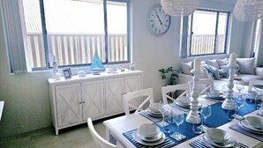 Un coin repas avec une nappe bleue, des chaises blanches et un buffet blanc agrémenté d’objets décoratifs.