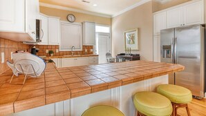 A kitchen with white cabinets, a stainless steel refrigerator, a tiled island, and a clock on the wall. - Dog Friendly! 5 bedroom, 3 bath house near the MarshWalk (Murrells Inlet)