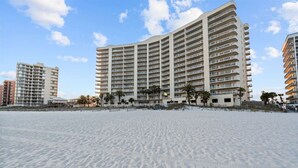 A beachfront hotel with multiple floors, a sandy beach in the foreground, and palm trees around. - Admiral Quarters Luxury Condo Gulf Front - Remodel (Orange Beach)