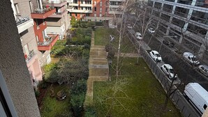 Un edificio residencial alto con varios balcones, un pequeño patio con árboles y un estacionamiento con coches.