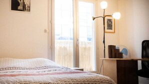 Un dormitorio con cama, escritorio, silla, lámpara y ventana con persianas.