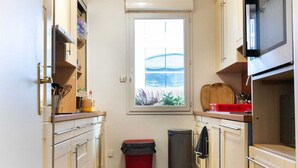 Una cocina estrecha con armarios blancos, un ventanal con vistas, un microondas y un cubo de basura.