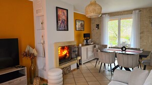 Un salon avec une cheminée, un coin repas avec une table et des chaises, et un téléviseur posé sur un meuble en bois.