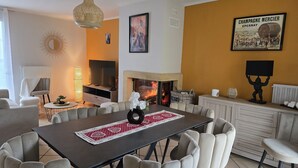 Un salon moderne avec une cheminée, une table à manger avec des chaises, un téléviseur et des objets décoratifs.