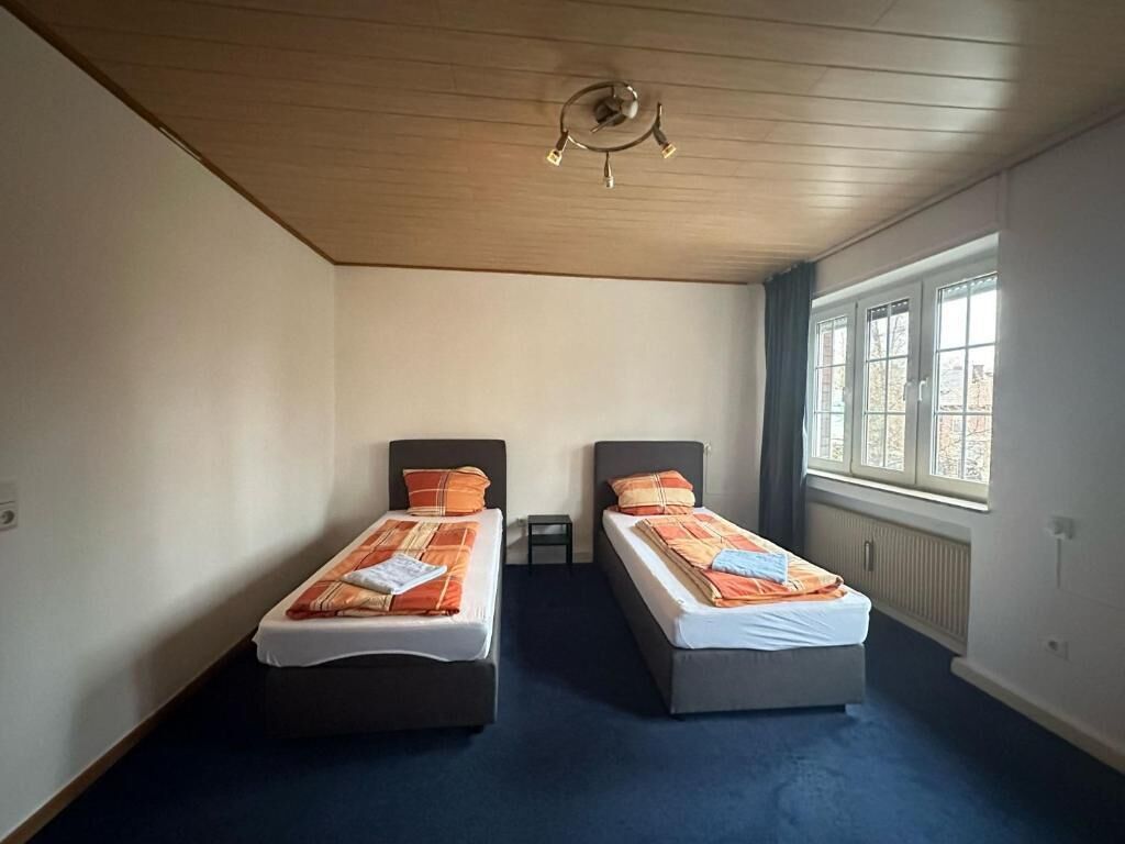 Una habitación con dos camas individuales, techo de madera, ventana con vistas y un radiador.