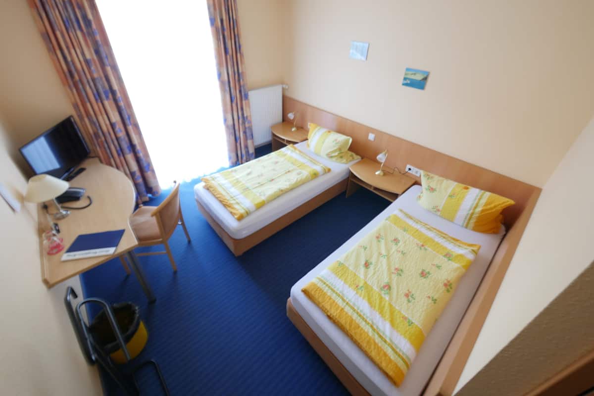 Een hotelkamer met twee bedden, een bureau met een computer, een stoel en een kleine tafel.