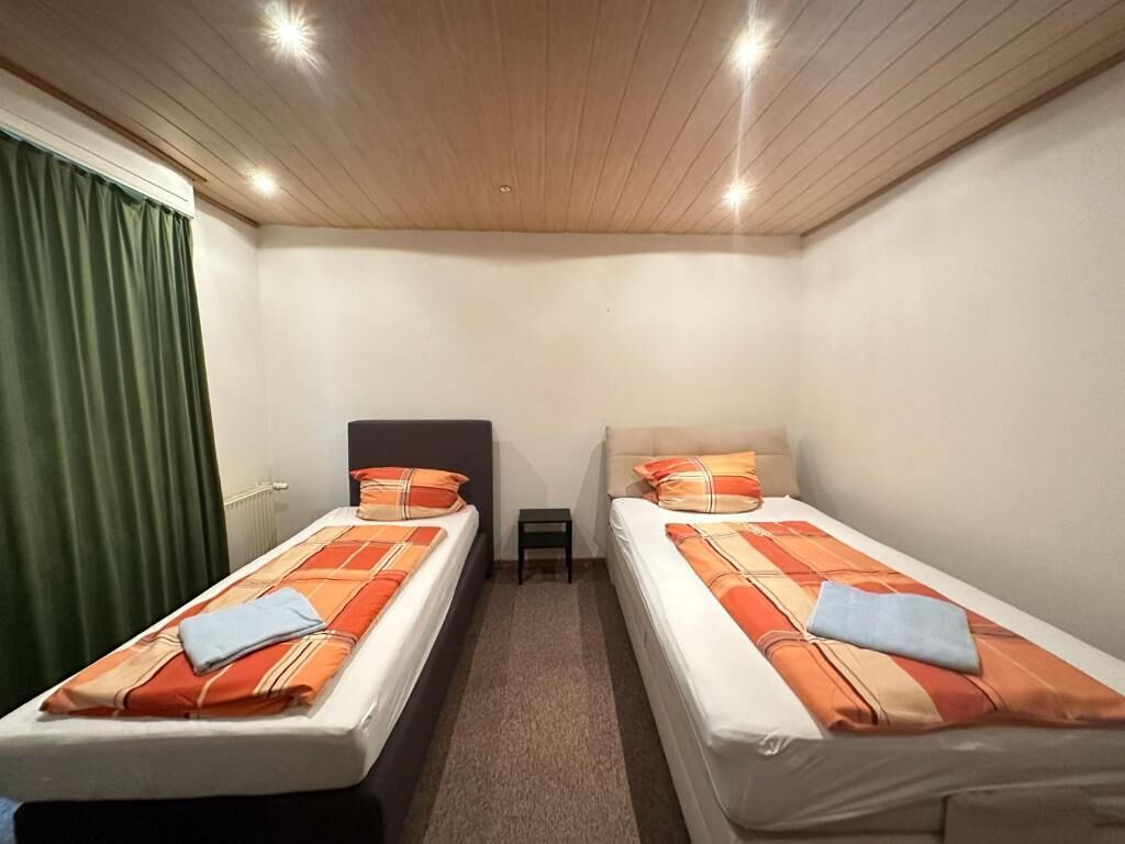 A room with two single beds, a small table, and a ceiling with recessed lighting.