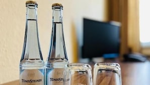Twee flessen TonicSteiner Classic en TonicSteiner Clean op een houten tafel met vier lege glaasjes.