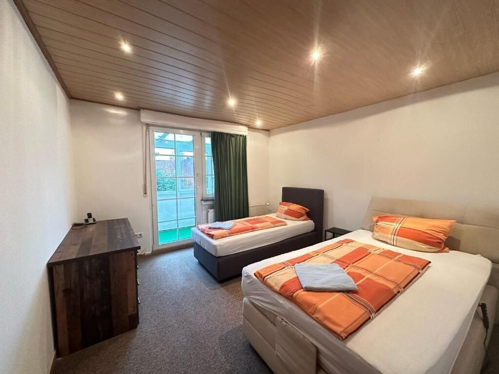 A bedroom with two beds, a wooden ceiling, a small desk, and a sliding glass door leading to a balcony.