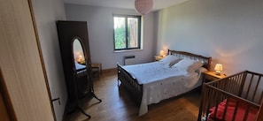 Une chambre à coucher avec un lit, une commode en bois, un miroir, une fenêtre et un berceau.