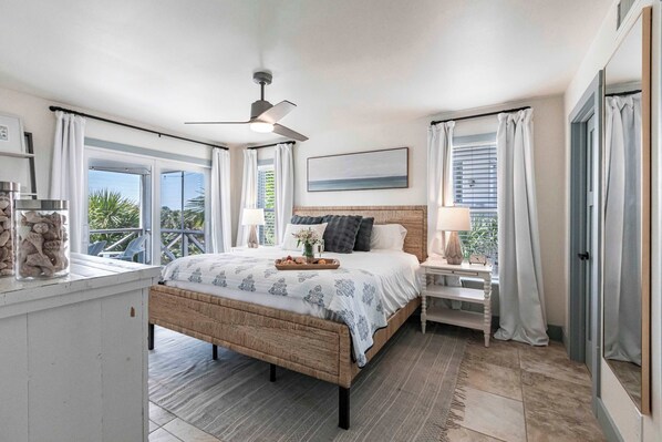 A bedroom with a bed, bedside tables, a ceiling fan, and a view of the outdoors.