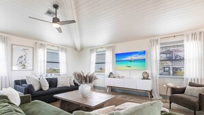 A spacious living room with a large sofa, a coffee table, and a television displaying a scenic ocean view. - Shellabration: Ocean Views, Heated Pool, Basketball, Golf Cart (North Captiva)