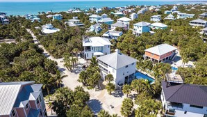 An aerial view of a coastal residential area with houses, a swimming pool, and palm trees. - Shellabration: Ocean Views, Heated Pool, Basketball, Golf Cart (North Captiva)