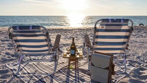 Two striped beach chairs facing the ocean with a bottle and glasses on a small table between them. - Shellabration: Ocean Views, Heated Pool, Basketball, Golf Cart (North Captiva)