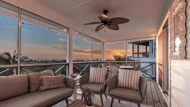 A balcony with a sofa, chairs, and a table. There is a ceiling fan and a view of the sunset. - Shellabration: Ocean Views, Heated Pool, Basketball, Golf Cart (North Captiva)