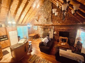 L’intérieur d’une cabane en rondins comprend une cuisine, un coin repas et un salon, avec des poutres en bois, des murs en pierre et une cheminée.
