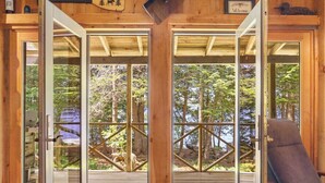 Una cabaña de madera con puerta de vidrio que da a una terraza, un letrero de bienvenida y una silla.