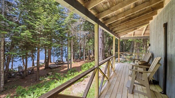 Una terraza de madera con sillas Adirondack, con vistas a un área boscosa y un lago.